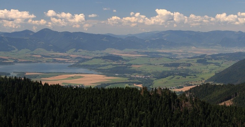 05-IMG 6518 -- Nieco dalej: połać Kotliny Liptowskiej ze zbiornikiem wodnym Liptovská Mara. Po lewej stronie wznoszą się Niżnie Tatry – zalesione grzbiety opadają od kopulastego Salatína. Białe budynki przy prawej krawędzi kadru to skrawek Ružomberoka. Miasto leży u stóp Wielkiej Fatry, którą od Niżnich Tatr oddziela dolina (niewidocznej stąd) Revúcy