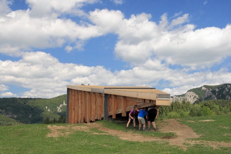 13-IMG 6792 -- Alberti zaproponował teoretyczny model postrzegania trójwymiarowej rzeczywistości i zarazem wyłożył metodę jej malarskiego odwzorowania. Właśnie u niego czytamy o "piramidzie widzenia": ustawionej "poziomo", jej wierzchołek znajduje się na wysokości oczu, podstawę stanowi plan obejmowany wzrokiem; powstały w ten sposób ostrosłup to wiązka nieskończenie wielu promieni, wychodzących od poszczególnych punktów podstawy i zbiegających się w źrenicy obserwatora. Dzieło malarza "jest więc [...] przekrojem piramidy widzenia, artystycznie przedstawionym na pewnej powierzchni za pomocą linii i barw, z uwzględnieniem określonej odległości, punktu centralnego i oświetlenia" (<i>De Pictura</i>, księga I, § 12 – <a href="http://www.ousia.it/SitoOusia/SitoOusia/TestiDiFilosofia/TestiPDF/Alberti/DePictura.pdf" target="_blank">LINK</a>, tłum. własne; schematyczna ilustracja: <a href="https://www.degruyter.com/view/j/semi.2015.2015.issue-207/sem-2015-0039/graphic/sem-2015-0039_figure1.jpg" target="_blank">LINK</a>). Teoria opiera się na założeniu, że obserwator trwa w tym samym miejscu. Włoski uczony przyrównał krawędzie płótna do framugi okna, przez które spoglądamy na świat. W XXI wieku Słowak Juraj Gábor poszedł jeszcze dalej i... nadał abstrakcyjnej piramidzie widzenia całkiem konkretną, bo drewnianą, sporych rozmiarów postać – ukazaną na powyższym zdjęciu (wraz z kolejką niecierpliwych koneserów-imaginatorów)