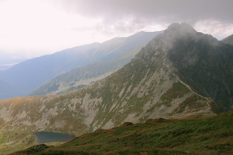 033-IMG 4358 -- Dochodząca tu od południowego wschodu główna grań zakręca na południe, by po drugiej stronie głębokiej przełęczy
poderwać się (patrz: zdjęcie) do góry i przybrać formę skalistego grzebienia. Po lewej można dostrzec taflę Jamnickiego
Stawu Wyżniego (Vyšného Jamníckeho plesa)