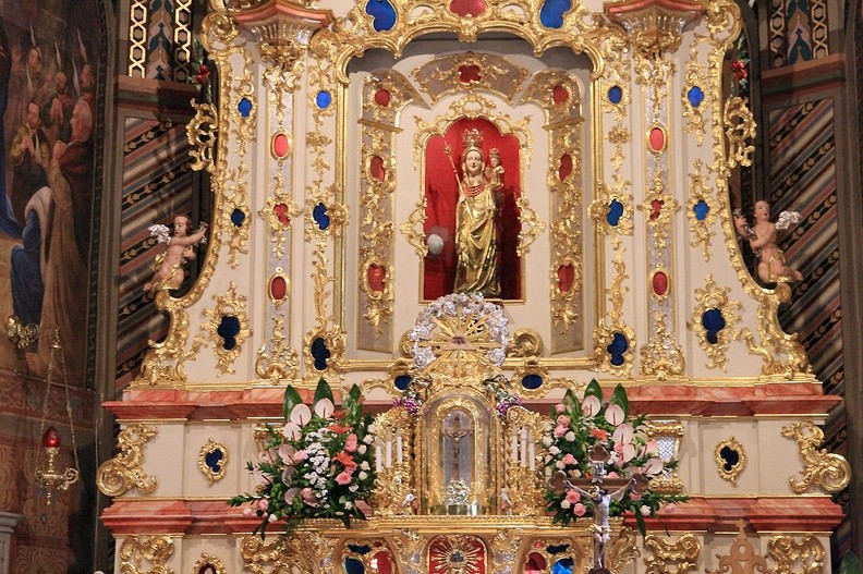 06-IMG 3389 -- Rzeźba Matki Boskiej Ludźmierskiej pochodzi z około 1400 roku. Jak opowiedziała pani Antonina z Ludźmierza: "Dawno temu jechał tędy kupiec i ugrzązł w bagnach. Mówi więc: Matko Boska, ratuj mnie. I uwidział na bagnie figurkę, jedzie za nią i nie utonął. Do brzegu dojechał, to mu zniknęła, ale wcześniej określił se jak wyglądała. Wyrzeźbił i wziął do siebie. Ale tam mu coś nie dało zostawić, więc przywiózł z powrotem do Ludźmierza i zostawił w kościele u cystersów" (Krzysztof Strauchmann, <i>Tajemnice skalnej ziemi</i>, Pruszków 2001,
s. 44). Według Pieńkowskiej i Staicha, więź górali z tą figurą nie wynika tylko z "wyróżnienia" jej przez Kościół. Sekret tkwi "w uśmiechu Matki": "spogląda ku nam twarz ludzka, dobra, głęboko macierzyńska i bardzo bliska. Konwencja stylowa, widoczna w głęboko ciętych, dekoracyjnych fałdach, w układzie korpusu, w nieco archaizującym i sztywnym ułożeniu Dzieciątka topnieje w zetknięciu z ludzką twarzą" (<i>Drogami...</i>, s. 155). Plik ze zdjęciem: <a href="http://www.dziennikgorski.type.pl/zdjecia/pojedyncze/IMG_3389.jpg" target="_blank">LINK</a>