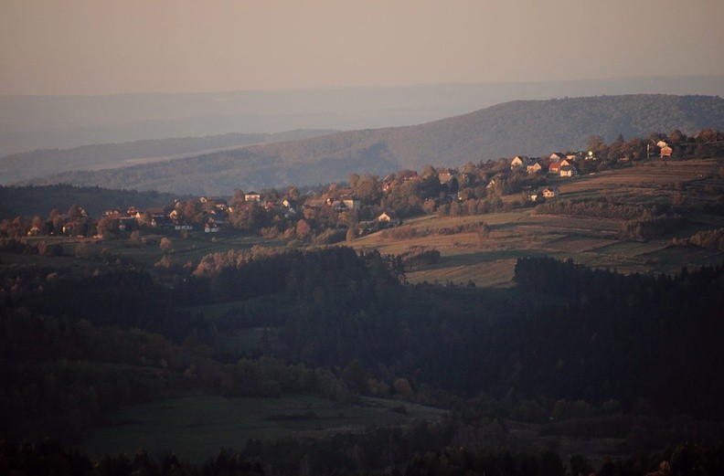 71-IMG 5073 -- Krzeszów Górny z Jaroszowicką Górą w tle. Po powrocie do Chatki zastaniemy koty śpiące na półce na werandzie, jeden na drugim. Maciej będzie uczył Mikołaja, jak rąbać drewno – Mikołaj pierwszy raz w życiu chwyci za siekierę (pod okiem Fachowca, przy zachowaniu zasad BHP). Przekąsimy coś, pogawędzimy i w szarówce, z żalem rozpoczniemy schodzenie. Obierzemy własny wariant, pochaszczujemy
w ciemnościach. Na ostatnim odcinku do auta poprowadzi nas Mikołaj. Fotografia w nieco większym rozmiarze: <a href="http://www.dziennikgorski.type.pl/zdjecia/pojedyncze/IMG_5073.jpg" target="_blank">LINK</a>